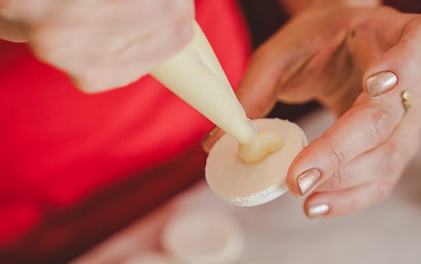 Piping cream onto a macaron shell during a Paris macaron-making workshop.
