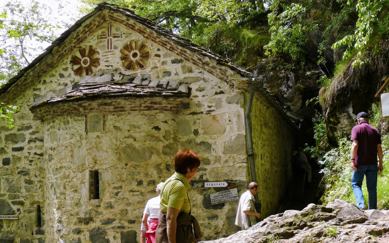 Guests entering St. Ivan Cave near a historic stone building surrounded by greenery.