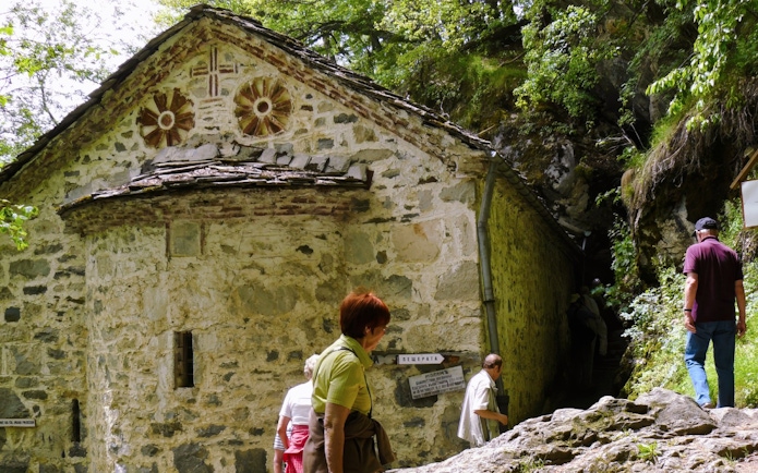 Guests entering St. Ivan Cave near a historic stone building surrounded by greenery.