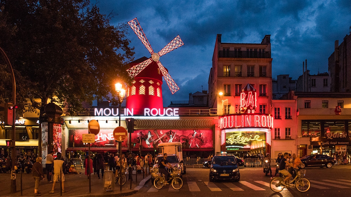 Moulin Rouge Paris exterior illuminated at night with vibrant lights and iconic windmill.