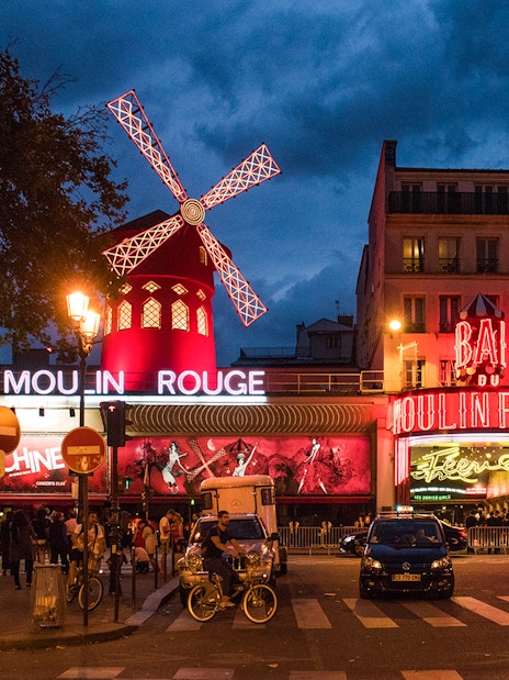 Panoramic view of Moulin Rouge exterior in Paris at night with illuminated windmill.