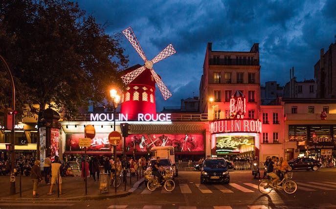 Panoramic view of Moulin Rouge exterior in Paris at night with illuminated windmill.