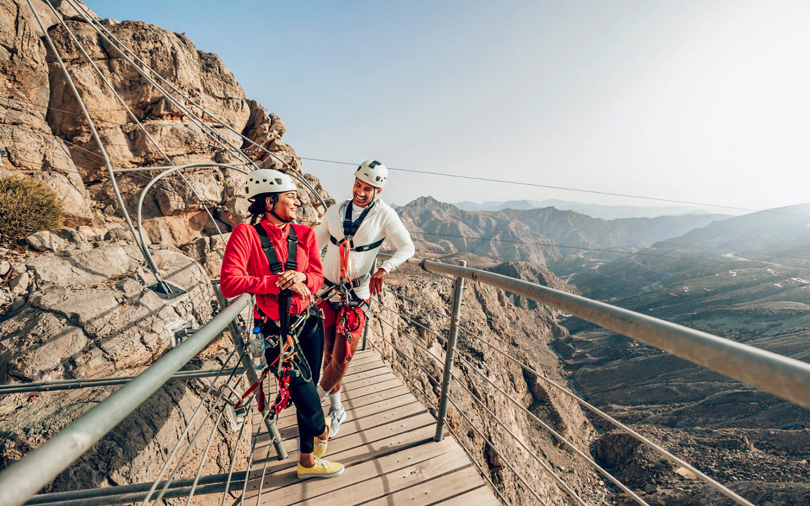 Two people in harnesses on a mountain zipline platform at Jais, UAE.