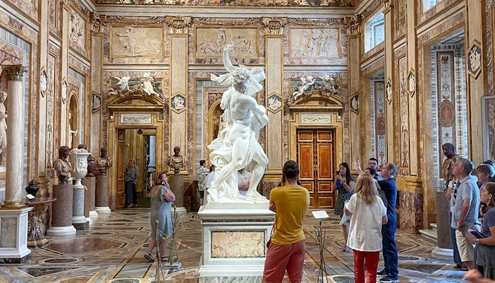 Sculpture of The Rape of Proserpina in Borghese Gallery, Rome, surrounded by visitors.