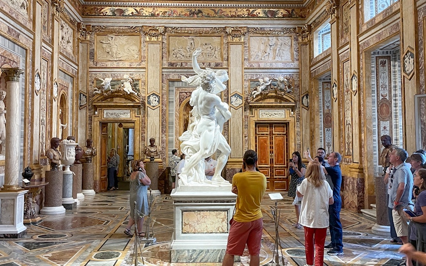 Sculpture of The Rape of Proserpina in Borghese Gallery, Rome, surrounded by visitors.