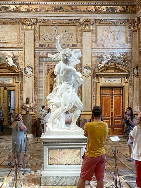 Sculpture of The Rape of Proserpina in Borghese Gallery, Rome, surrounded by visitors.