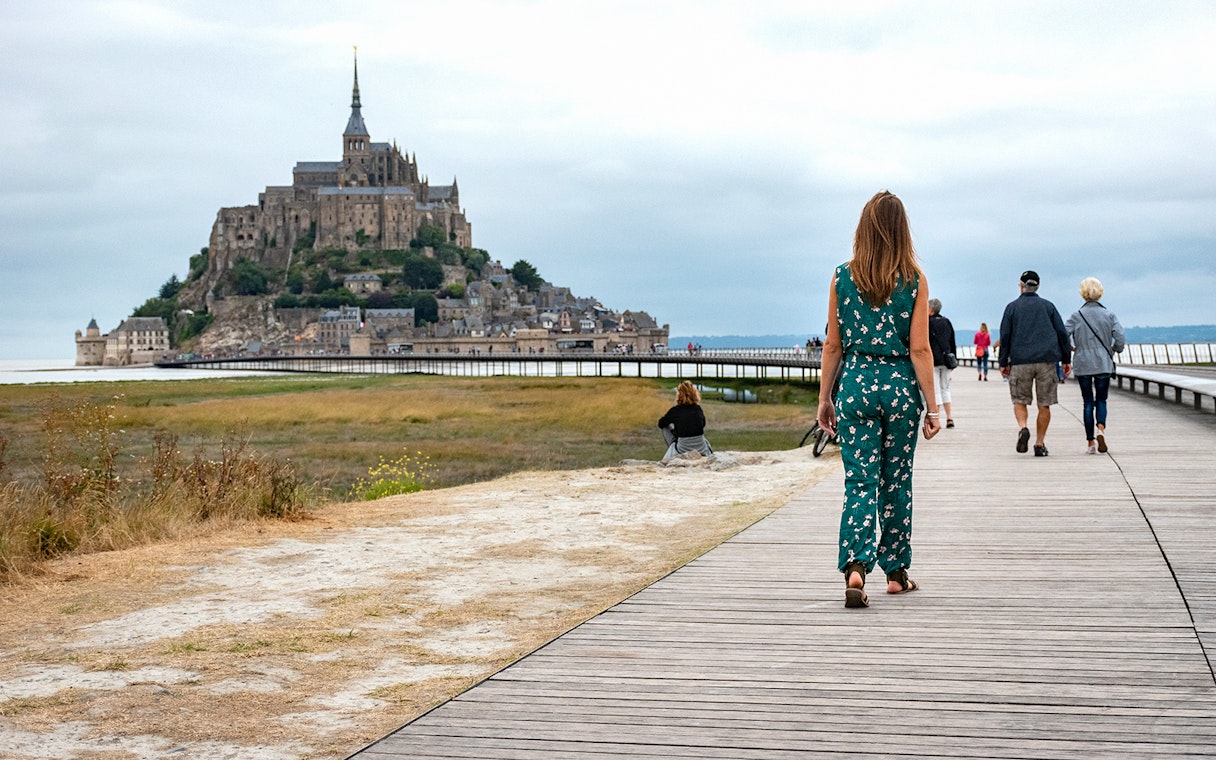 Visitors walking on a boardwalk towards Mont Saint-Michel in France.