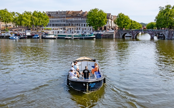 Small open boat cruising Amsterdam canal with passengers, historic buildings, and arched bridge in view.