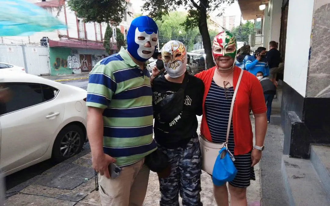 Three people wearing Lucha Libre masks outside Arena Mexico.