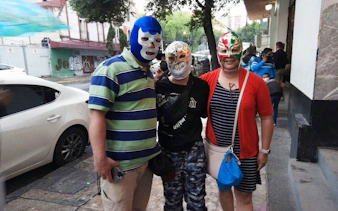 Three people wearing Lucha Libre masks outside Arena Mexico.