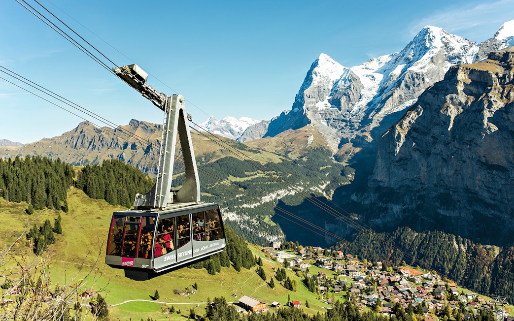 Cable car ascending in the Swiss Alps with views of snow-capped peaks and a village below, Swiss Travel Pass Flex.
