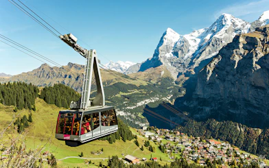 Cable car ascending in the Swiss Alps with views of snow-capped peaks and a village below, Swiss Travel Pass Flex.