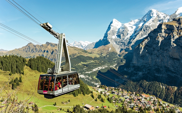 Cable car ascending in the Swiss Alps with views of snow-capped peaks and a village below, Swiss Travel Pass Flex.