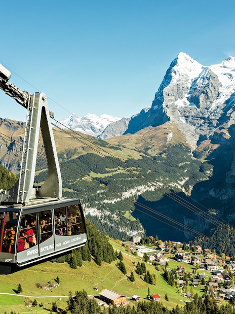 Cable car ascending in the Swiss Alps with views of snow-capped peaks and a village below, Swiss Travel Pass Flex.