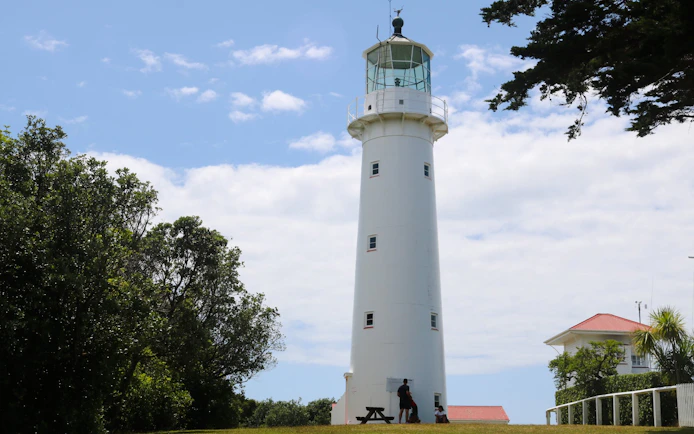 Lighthouse on Tiritiri Matangi Island with visitors, surrounded by trees and clear sky.