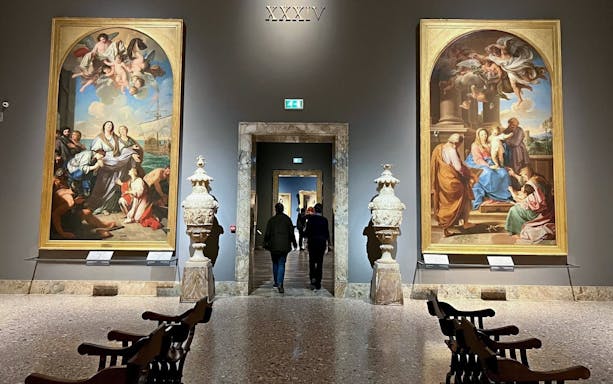 Visitors walking through the gallery at Pinacoteca di Brera, Milan, with classical paintings displayed.