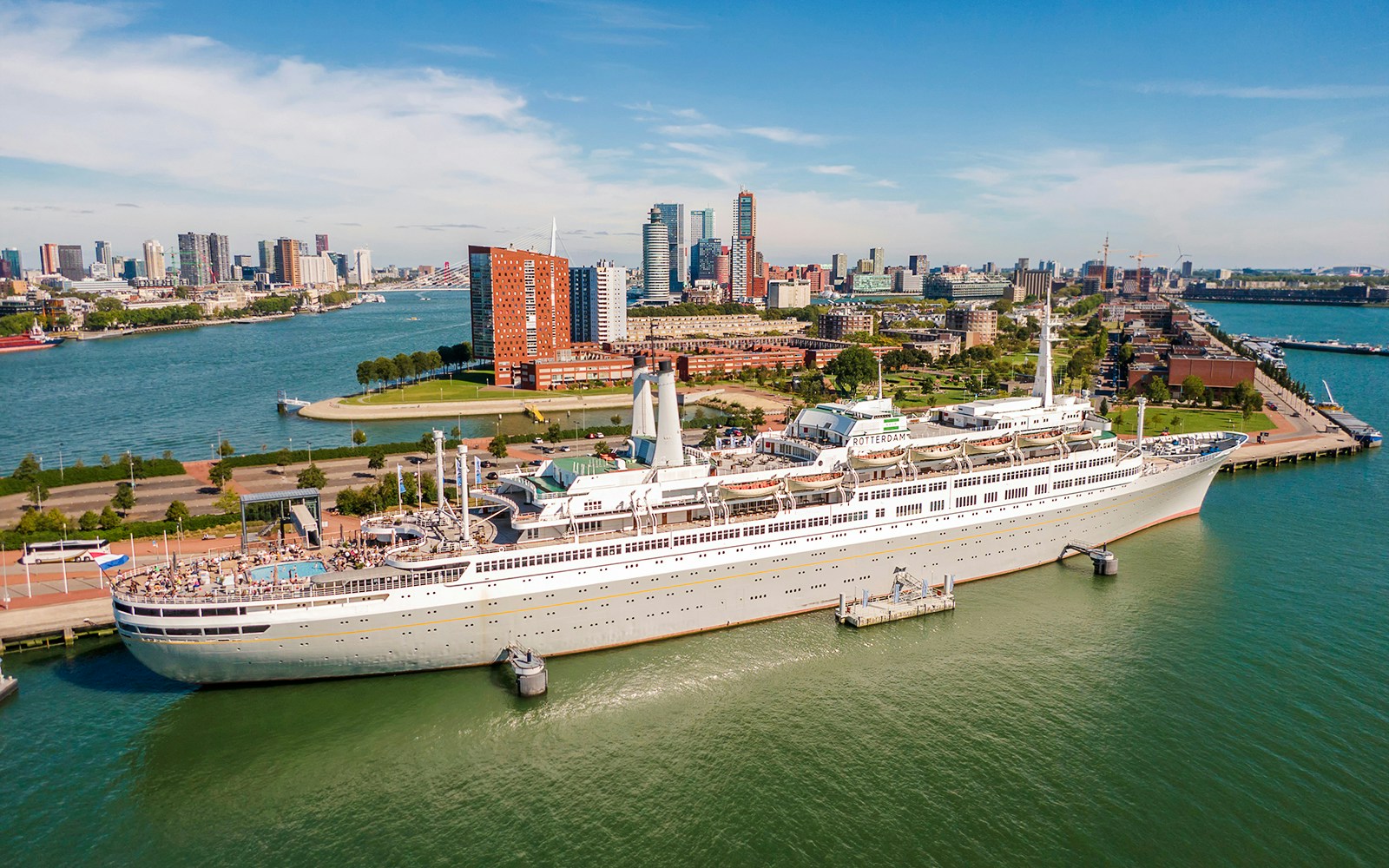 SS Rotterdam docked in Rotterdam harbor with city skyline in the background.