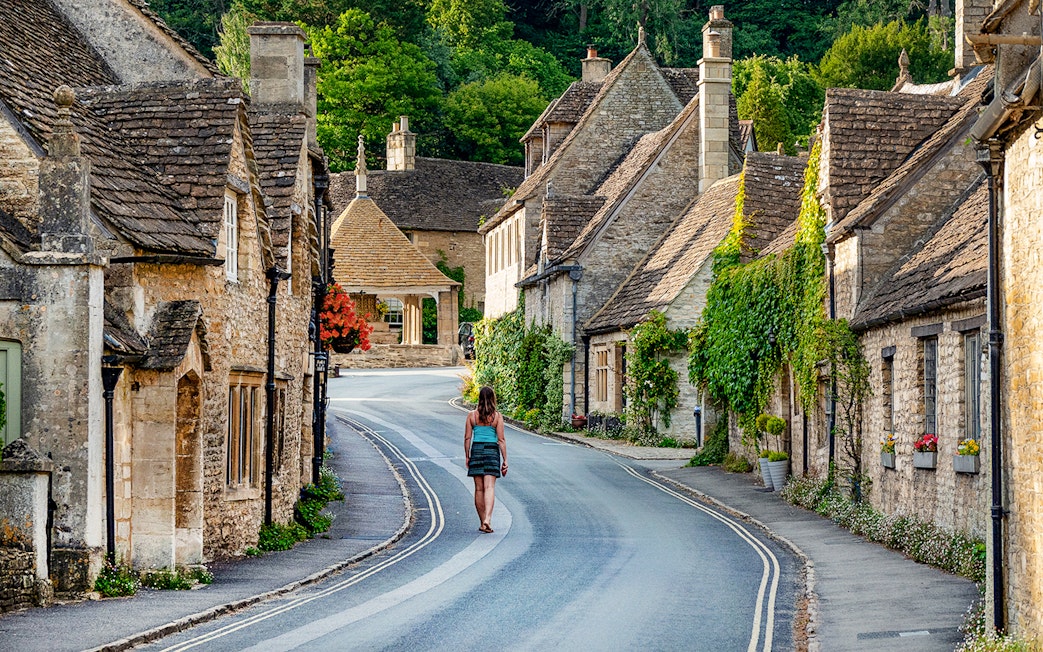 Cotswolds village street with stone cottages and a person walking, Oxford tour.