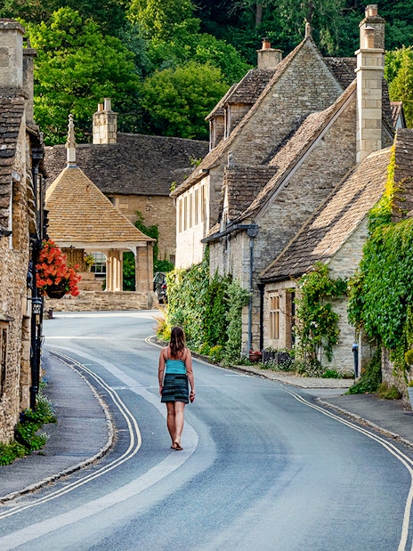 Cotswolds village street with stone cottages and a person walking, Oxford tour.