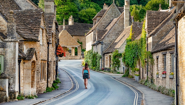 Cotswolds village street with stone cottages and a person walking, Oxford tour.