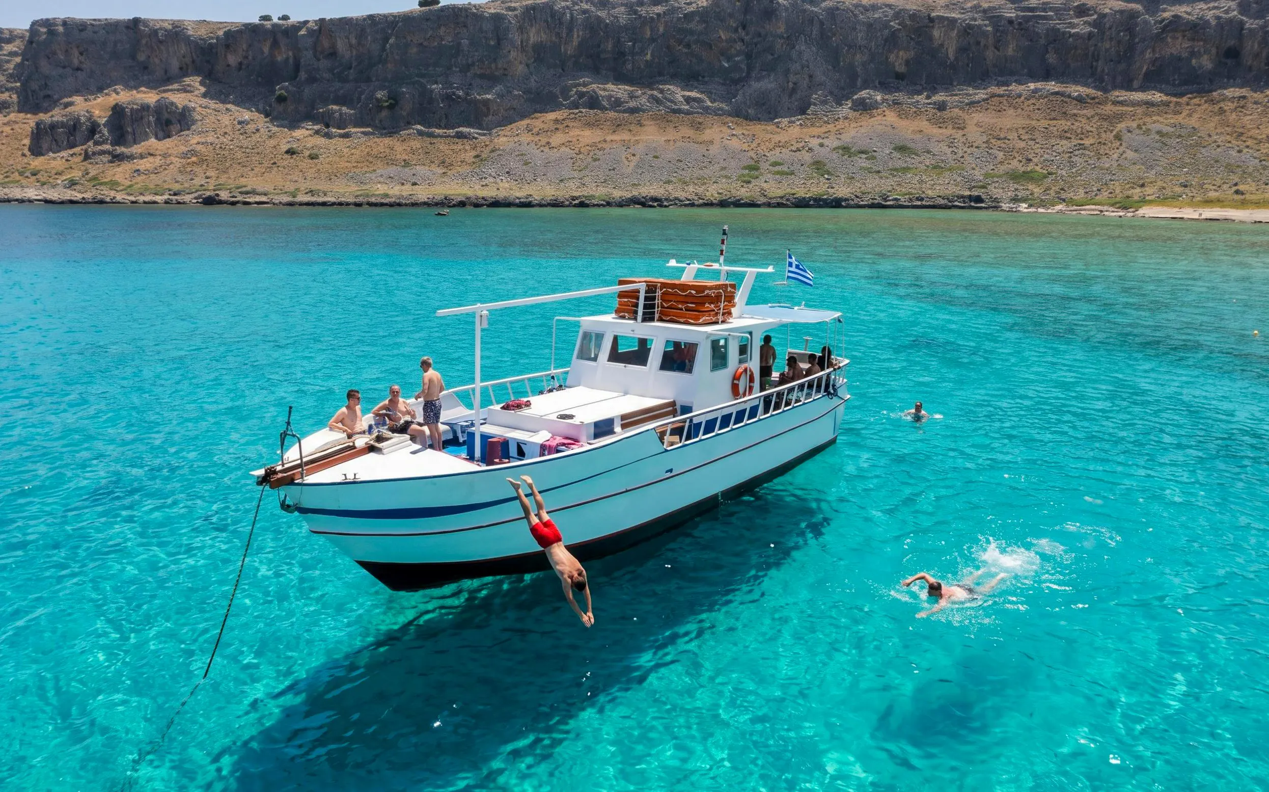Boat cruise with people swimming and diving in clear waters near Lindos, Pefkos.