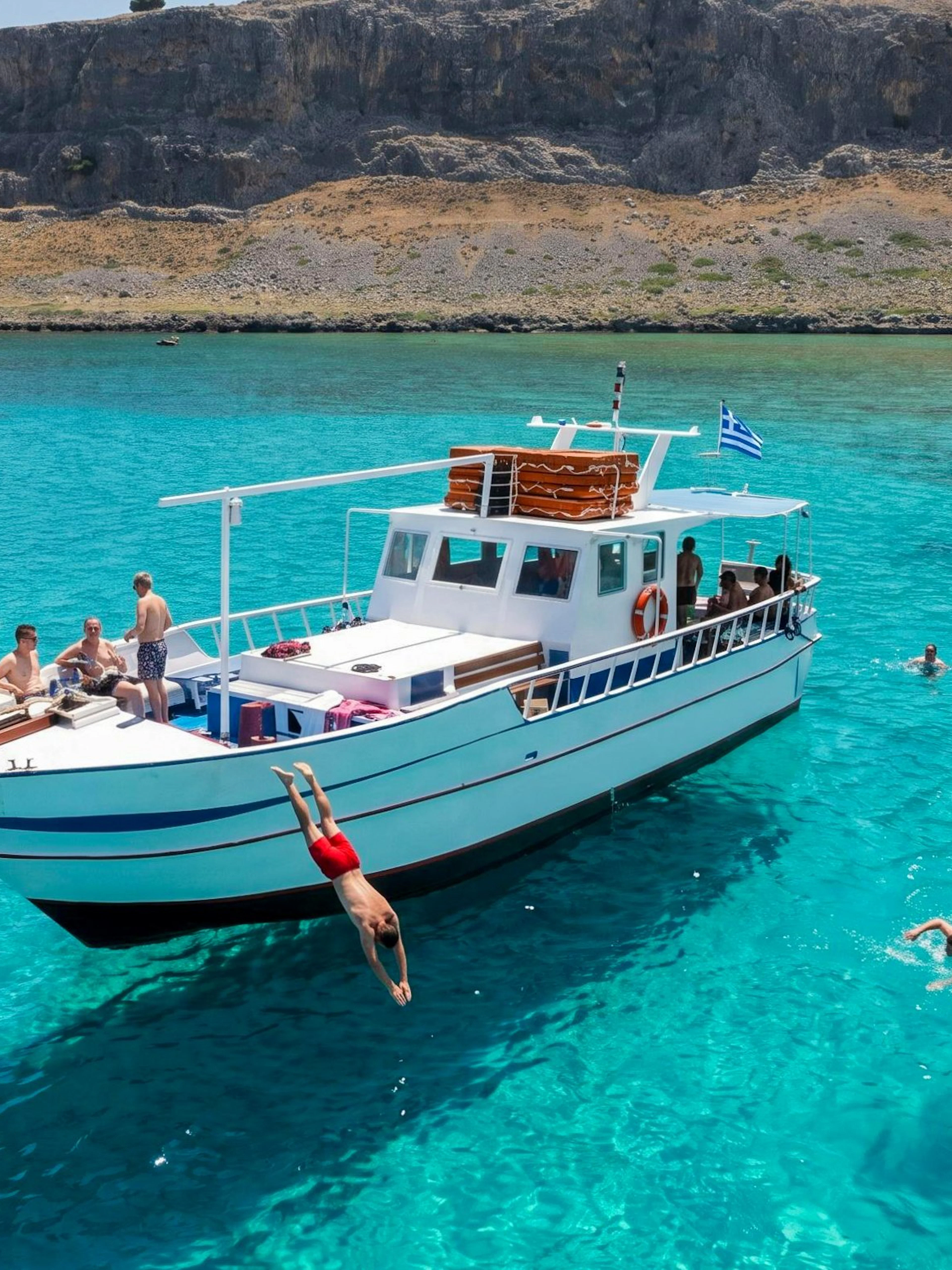 Boat cruise with people swimming and diving in clear waters near Lindos, Pefkos.
