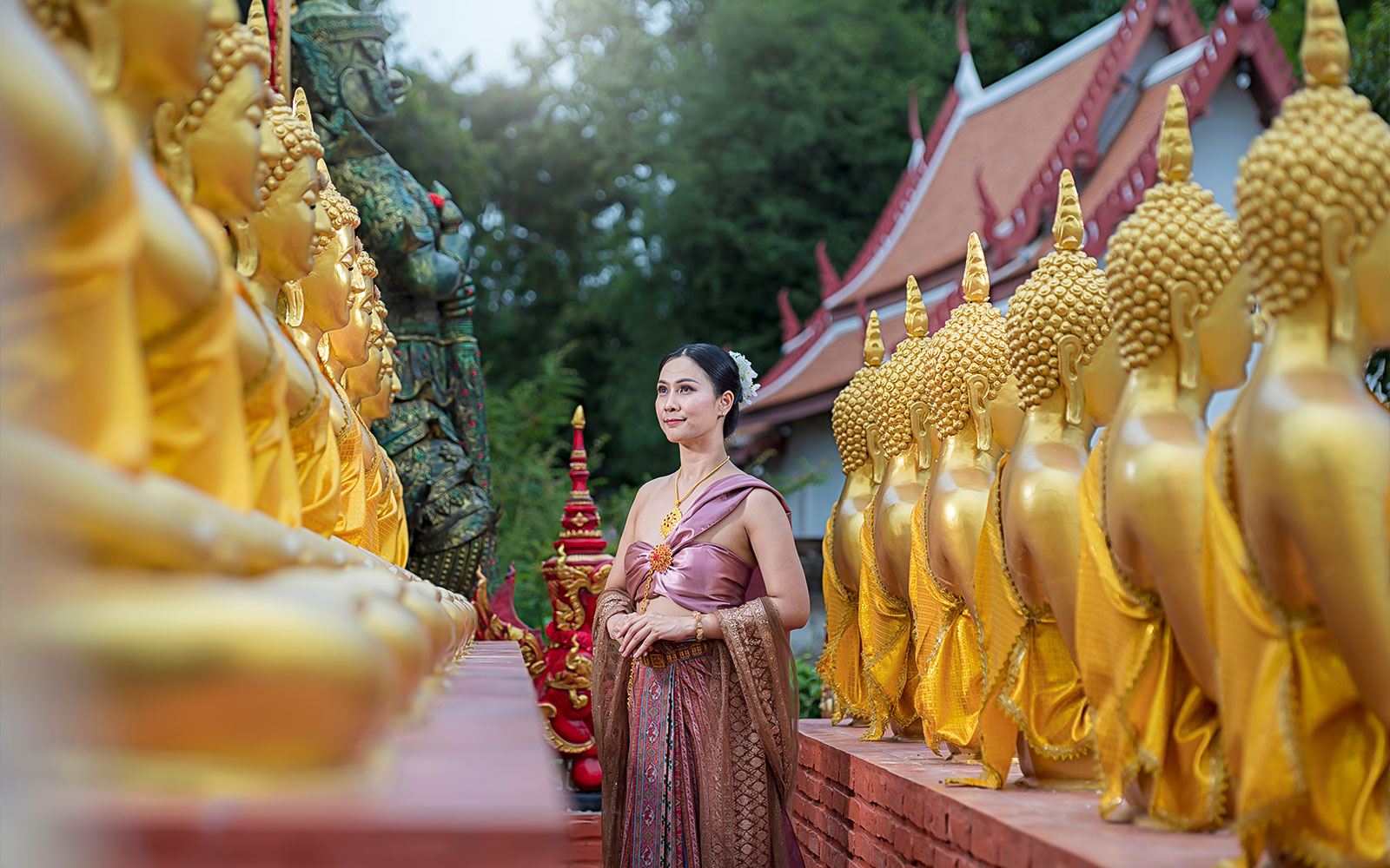 Woman in traditional attire walking between golden Buddha statues at an ancient city temple.