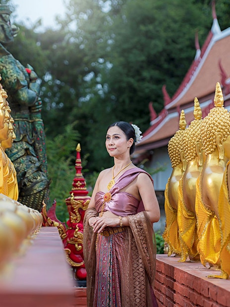 Woman in traditional attire walking between golden Buddha statues at an ancient city temple.