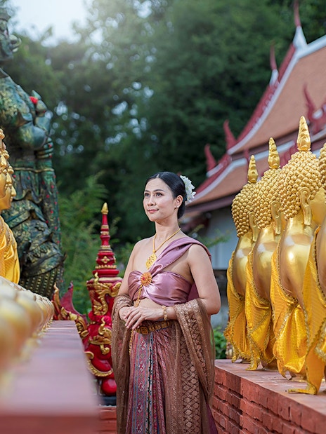 Woman in traditional attire walking between golden Buddha statues at an ancient city temple.