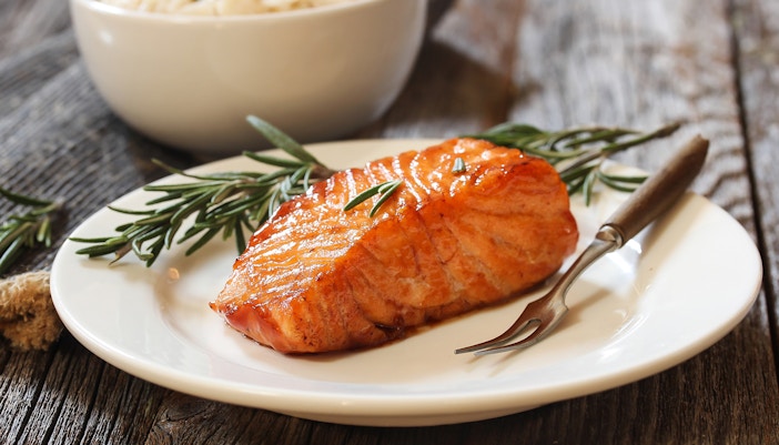 Honey sriracha glazed salmon with rosemary garnish on a white plate.