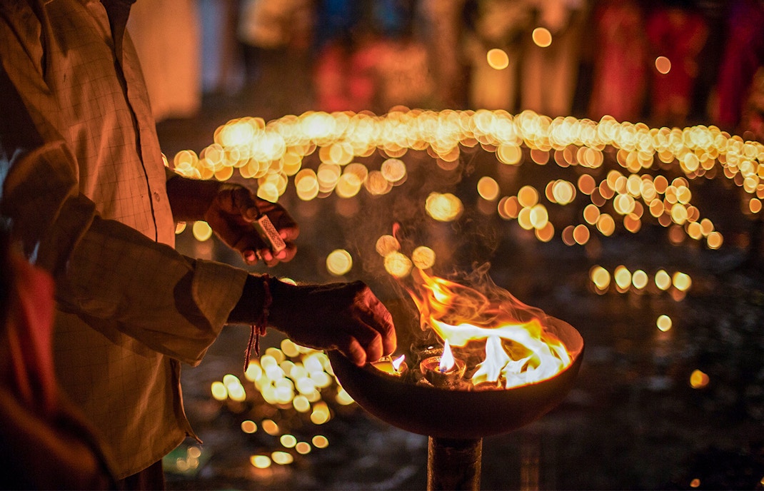 Person lighting oil lamps during Diwali celebration with bokeh lights in background.
