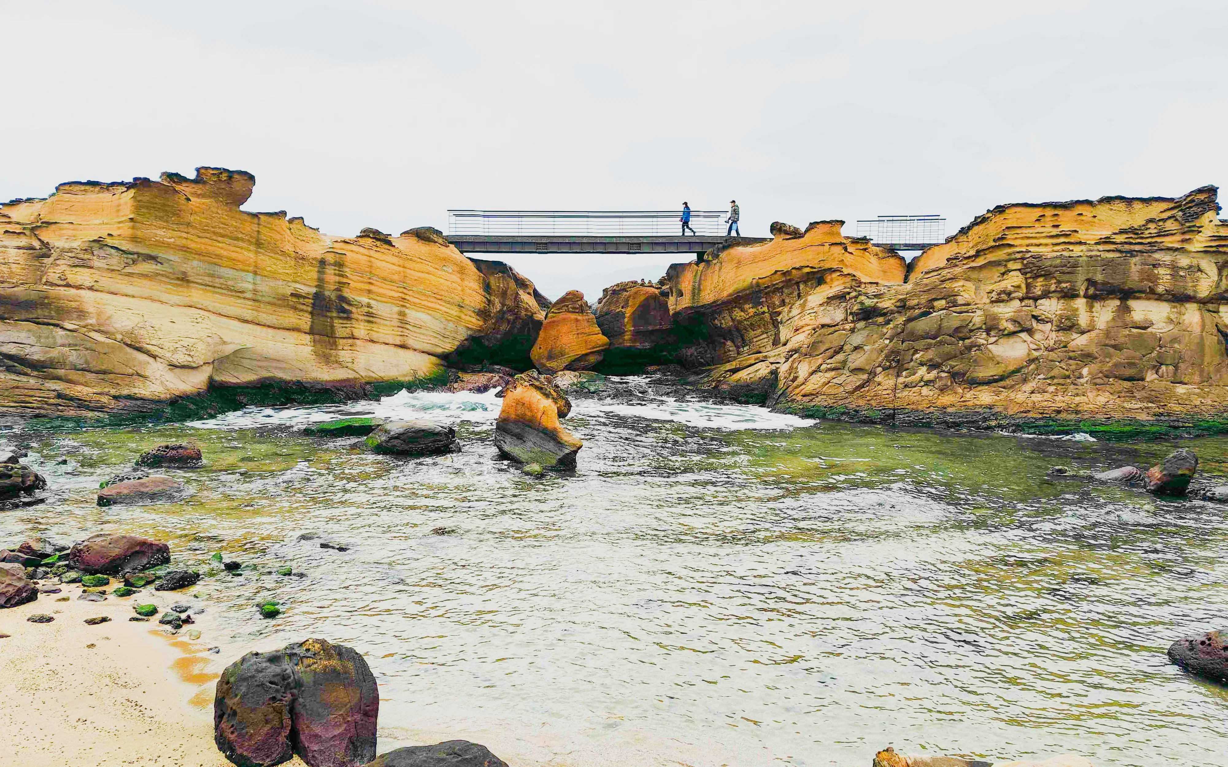Pedestrian footbridge over rocky inlet at Yehliu Geopark, New Taipei City, Taiwan.