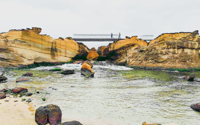 Pedestrian footbridge over rocky inlet at Yehliu Geopark, New Taipei City, Taiwan.