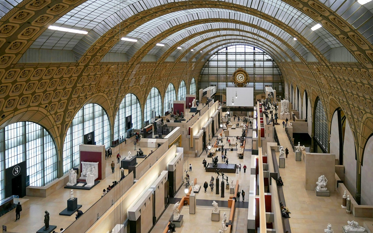 Panoramic view of the grand hall inside Musée d'Orsay, Paris, showcasing sculptures and visitors.