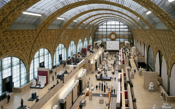 Panoramic view of the grand hall inside Musée d'Orsay, Paris, showcasing sculptures and visitors.