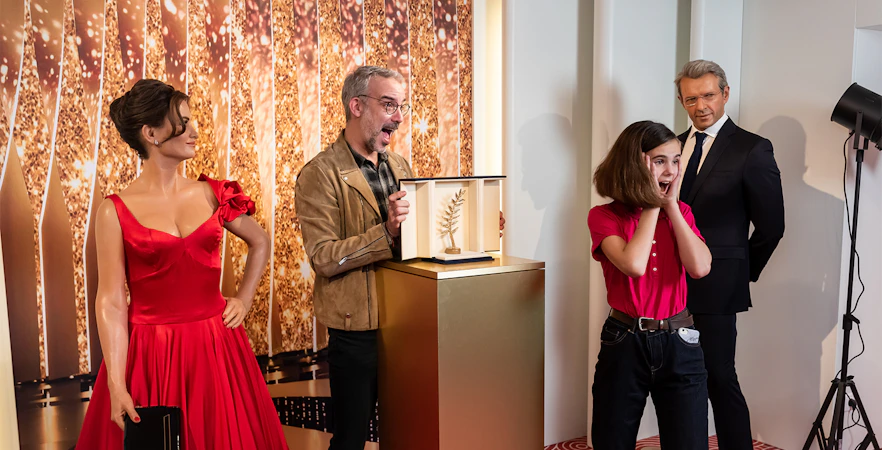 Grévin Wax Museum visitors admire wax figures and a Palme d'Or trophy display.