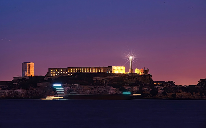 Alcatraz Island illuminated at night with ferry lights in San Francisco Bay.