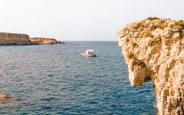 Boat on the sea near rocky cliffs during a guided tour in Syracuse.