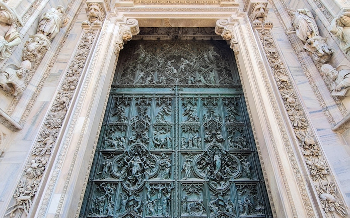 Ornate bronze door of Duomo Cathedral in Milan, featuring detailed religious carvings.