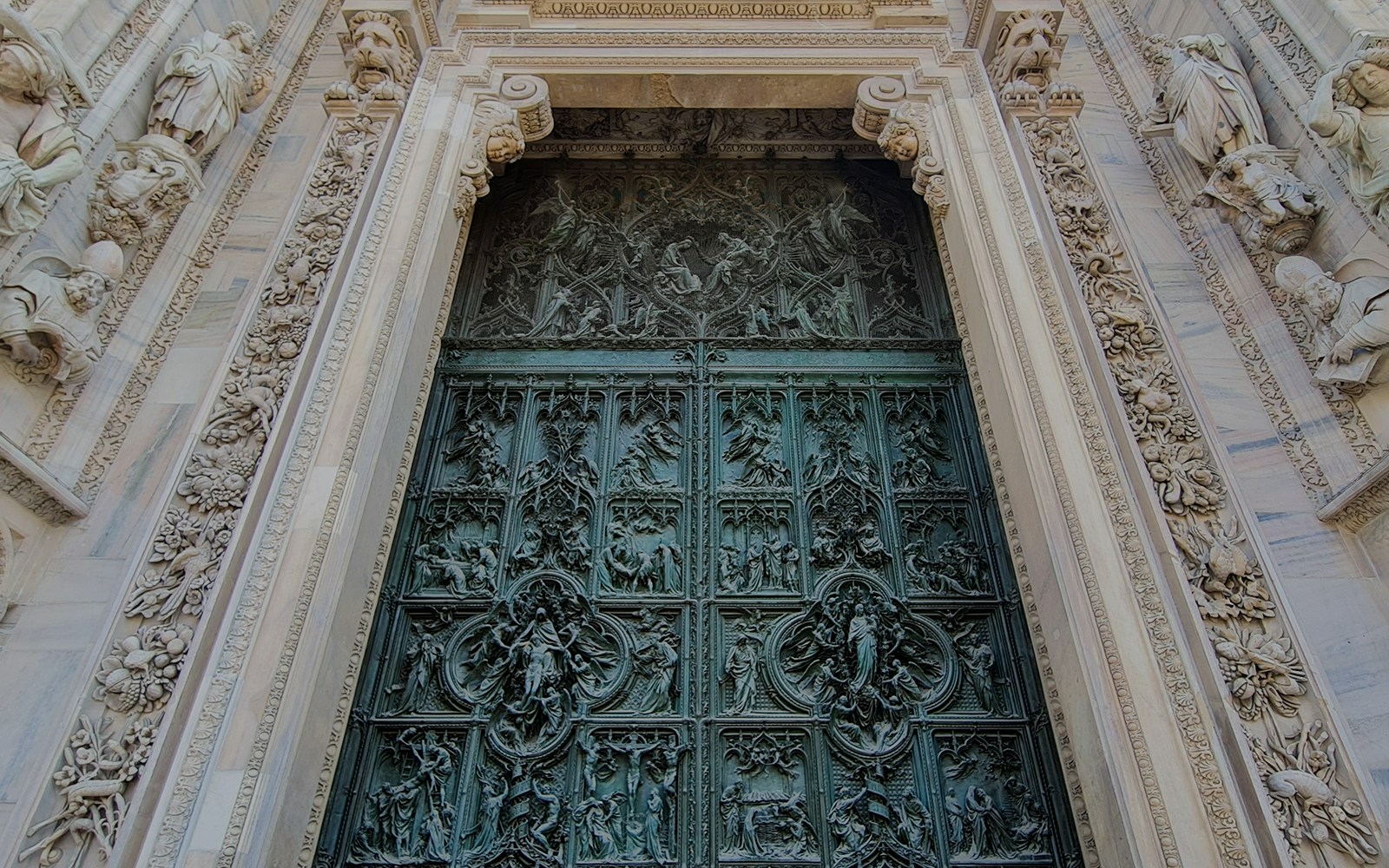 Ornate bronze door of Duomo Cathedral in Milan, featuring detailed religious carvings.