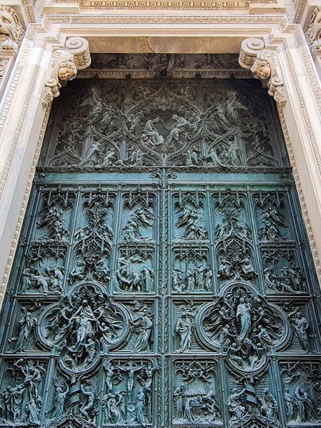 Ornate bronze door of Duomo Cathedral in Milan, featuring detailed religious carvings.