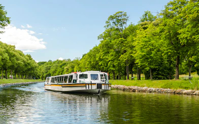 Cruise boat on Djurgården City Canal surrounded by lush green trees.