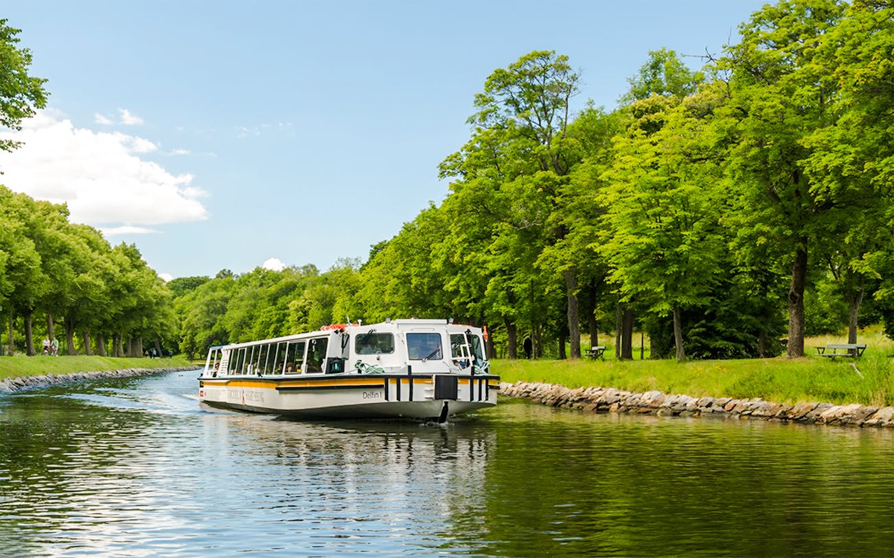 Cruise boat on Djurgården City Canal surrounded by lush green trees.