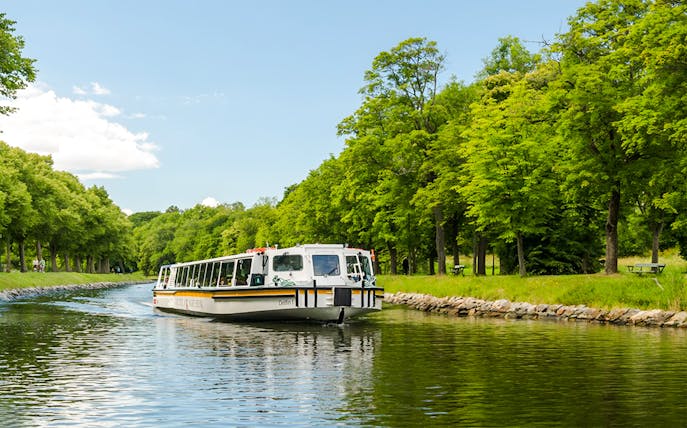 Cruise boat on Djurgården City Canal surrounded by lush green trees.