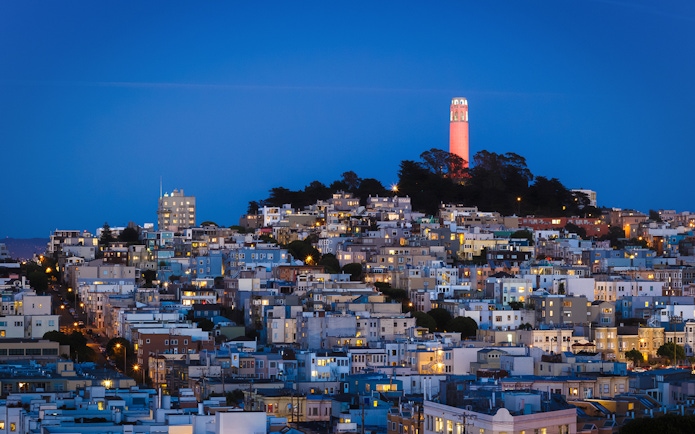 San Francisco skyline with Coit Tower illuminated at sunset.