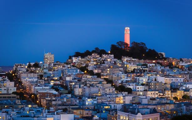 San Francisco skyline with Coit Tower illuminated at sunset.
