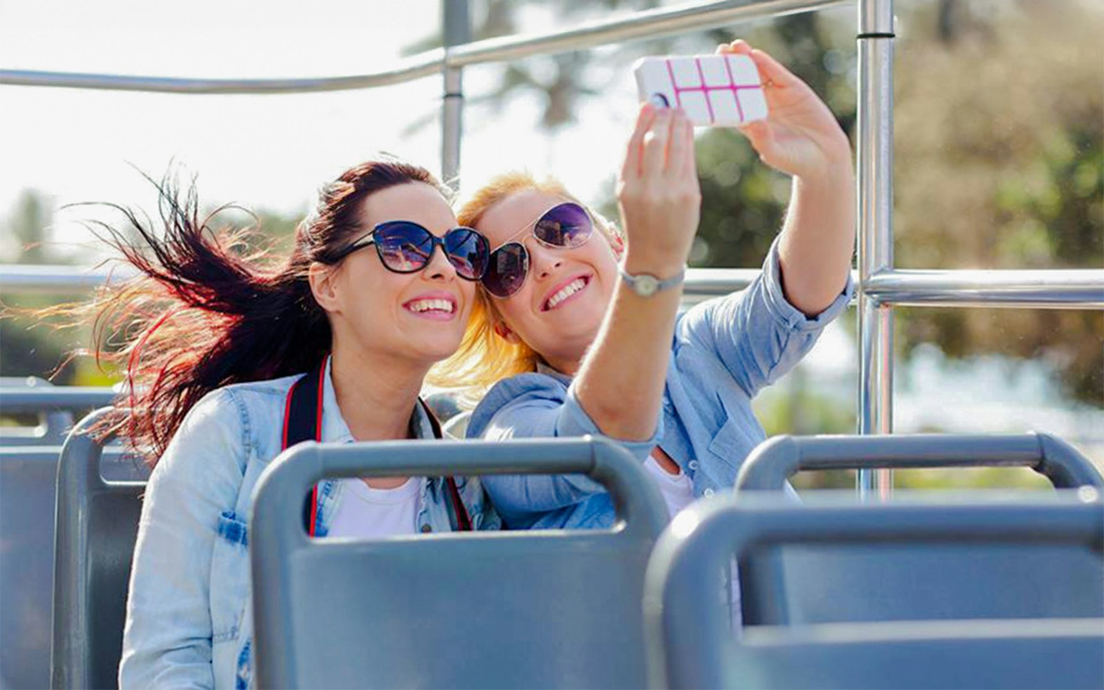 Two women taking a selfie on an open-top bus tour in Paris with the Eiffel Tower in the background.