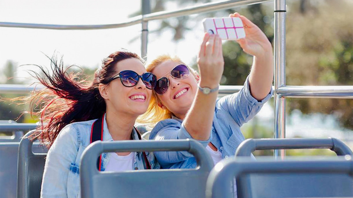 Two women taking a selfie on an open-top bus tour in Paris with the Eiffel Tower in the background.
