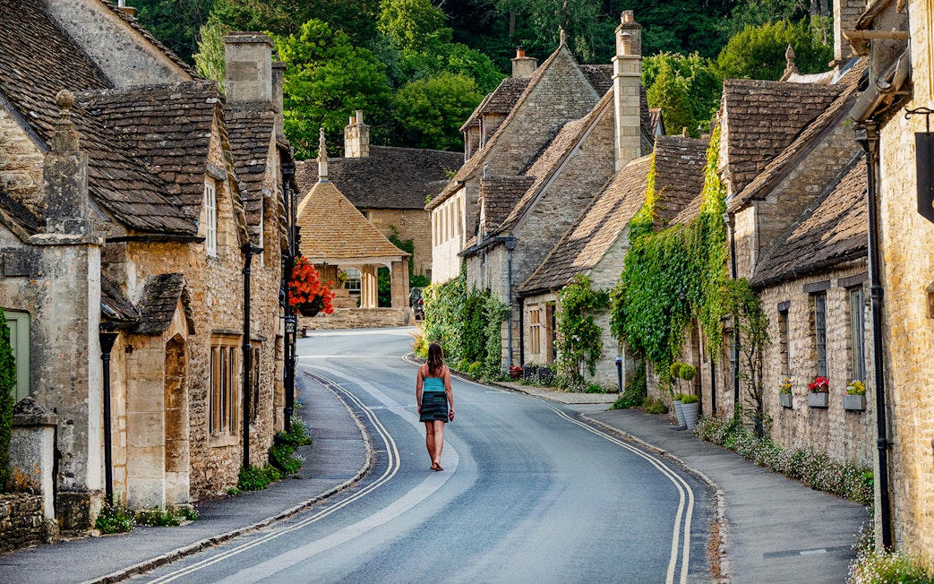 Tourist walking through a picturesque village street in the Cotswolds, England.