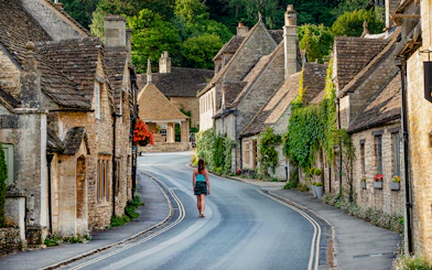 Tourist walking through a picturesque village street in the Cotswolds, England.